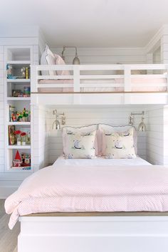 a white bunk bed with pink pillows in a room that has built - in bookshelves