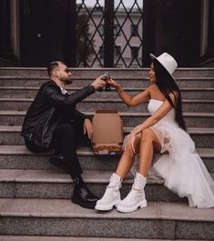 a man kneeling down next to a woman holding a wine glass in her hand while sitting on some steps