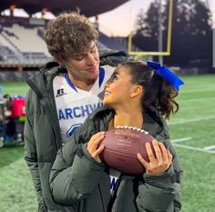 a woman holding a football while standing next to a man