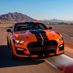 an orange and black car driving on a track with mountains in the background at sunset