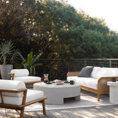 an outdoor living area with white furniture and potted plants on the deck, surrounded by greenery