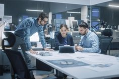 two men and a woman looking at a laptop in an office