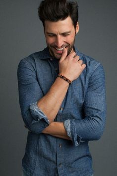 a man smiling and wearing a blue shirt with his hands on his chest, looking to the side