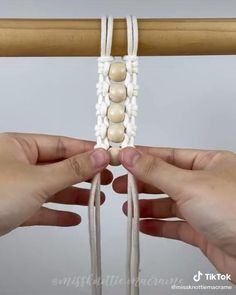 two hands are working on a beaded bracelet with white beads and wood dowels