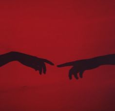 two hands reaching towards each other in front of a red background