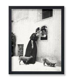 a black and white photo of a woman leaning against a wall with two small dogs