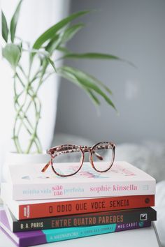 three books stacked on top of each other next to a potted plant and eyeglasses