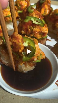 a person holding chopsticks over some food on a white plate with sauce and green peppers