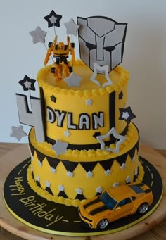 a yellow and black birthday cake with stars on it's sides, including a car