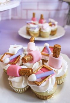 cupcakes decorated with pink, purple and gold icing on top of white plates