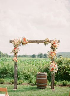 an outdoor ceremony setup with flowers on the arch and barrels in the grass behind it