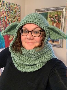 a woman wearing a crocheted yoda hat and scarf in front of paintings