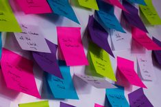 many post it notes are pinned to the wall with different colors and writing on them