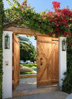 an open wooden door with flowers growing on it's sides and in between two white walls