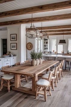 a large wooden table surrounded by chairs in a room with white walls and wood beams