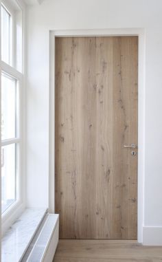 a wooden door in the corner of a room with white walls and wood flooring