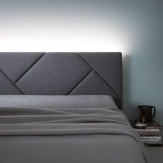 a bed with a gray headboard and two books on the nightstand next to it