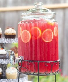 a glass jar filled with red liquid next to cupcakes