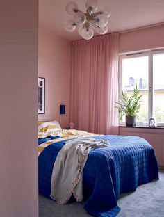 a bedroom with pink walls, blue bedding and a chandelier hanging from the ceiling