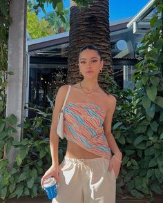 a woman standing in front of a palm tree holding a blue cup and wearing an animal print crop top