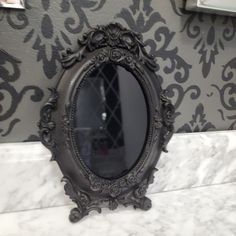 a mirror sitting on top of a marble counter next to a wallpapered wall