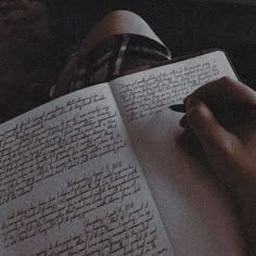 a person writing on an open book with a pen in their hand, while sitting down