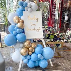 a baby shower sign surrounded by blue and gold balloons in a room with other decorations