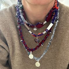 a woman wearing a multi - layer necklace with charms and beads on her neck is looking at the camera