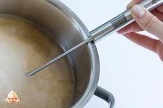 a person is stirring something in a pot with a ladle on the side and a stick sticking out of it