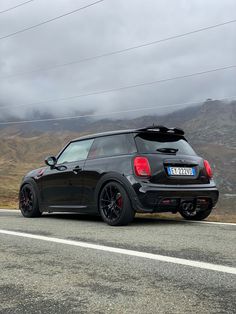 a small black car is parked on the side of the road with mountains in the background