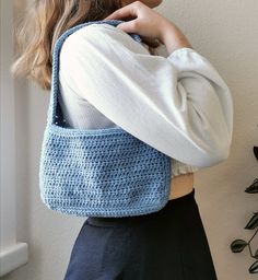 a woman wearing a blue crochet bag with her hand on her shoulder and looking down