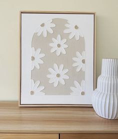 a white vase sitting on top of a wooden table next to a framed art piece