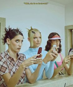 three women are looking at their cellphones while sitting on a ledge in front of them