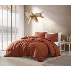 a bed with an orange comforter and pillows in a room next to a window