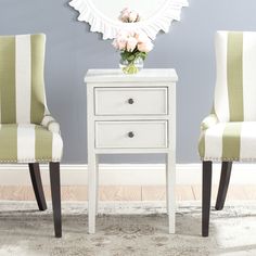 two chairs and a table in front of a wall with a flower vase on it