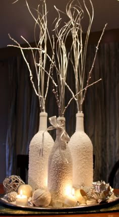 three white vases with branches in them on a tray decorated with candles and ornaments