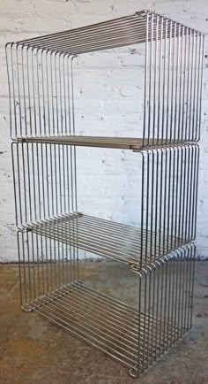 three tiered metal shelf against a white brick wall in an empty room with concrete flooring