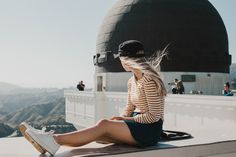 a woman sitting on the edge of a building looking at her cell phone