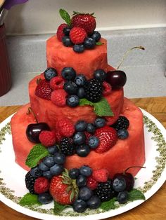 a watermelon cake with berries and mints on top is sitting on a plate