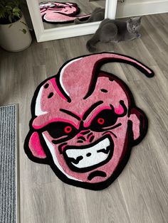 a cat sitting on the floor next to a pink rug with an angry face drawn on it