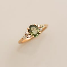 an oval green and white diamond ring with three smaller round diamonds on the band, set in yellow gold