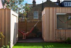 a person laying in a hammock between two wooden buildings on the side of a yard