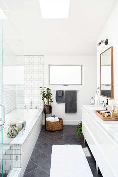 a white bathroom with two sinks and a bathtub next to a window in the ceiling