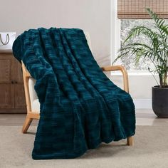 a green blanket sitting on top of a wooden chair next to a potted plant