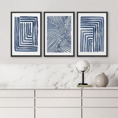 three blue and white paintings on a wall above a dresser