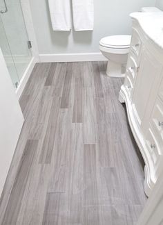 a white toilet sitting in a bathroom next to a walk in shower and wooden floors