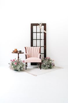 a pink chair sitting on top of a white floor next to a table with flowers