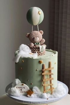 a birthday cake with a teddy bear on top and balloons in the sky above it