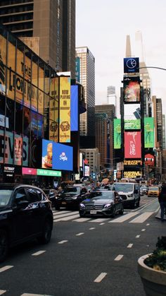 cars driving down a busy city street with billboards on the buildings in the background