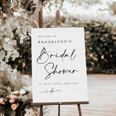 a sign that is standing up in front of some flowers and trees with the words brooklyn's bridal shower written on it